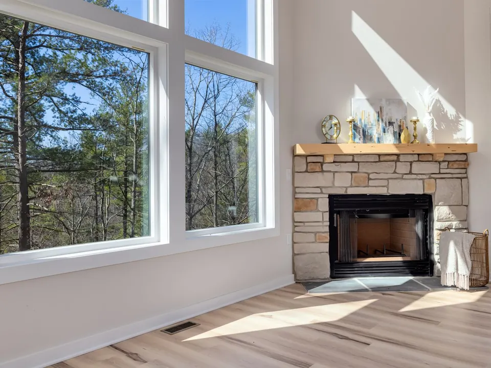 Sunlit living room with tall white picture windows looking onto pine trees